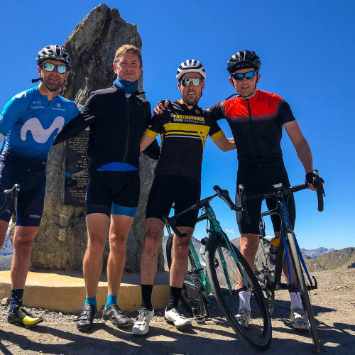 four cyclists pose at col de la bonette sign with alpine peaks backdrop on marmot tours cycling holiday in southern French alps