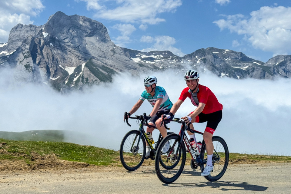 pair of cyclists summit col D'Aubisque with cloud inversion and mountain peaks backdrop in French pyrenees on marmot tours cycling holiday