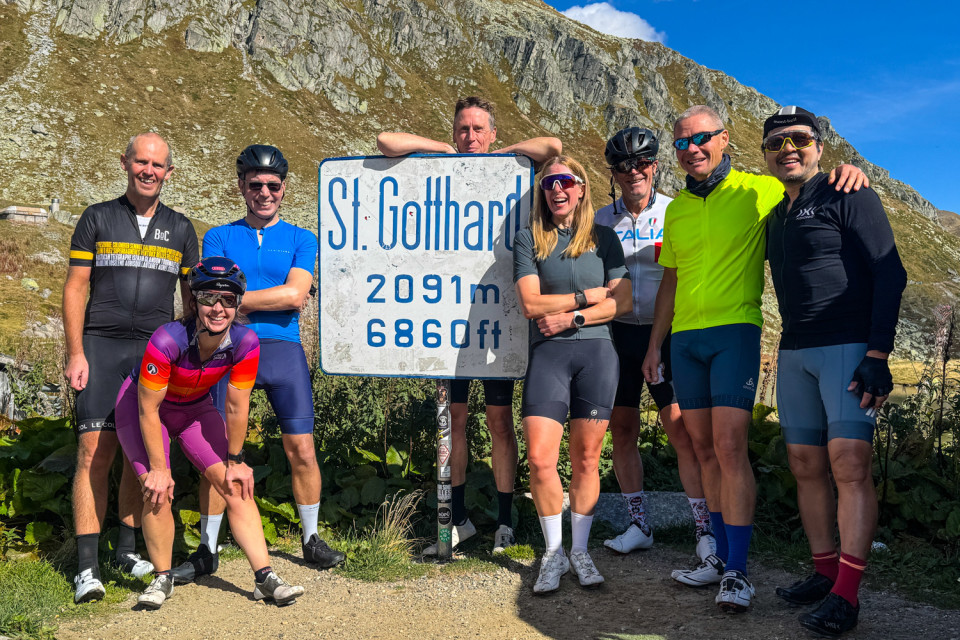group if cyclists pose at st gotthard pass sign on marmot tours guided road cycling tour Swiss alps
