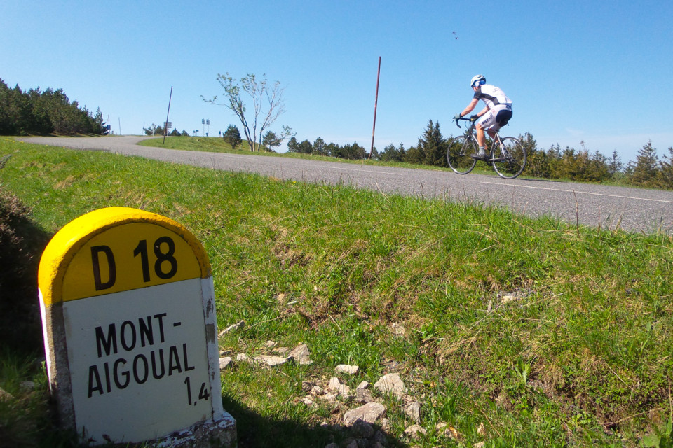 cyclist summiting mont aigoual alongside road marker on marmot tours guided road cycling holiday in France