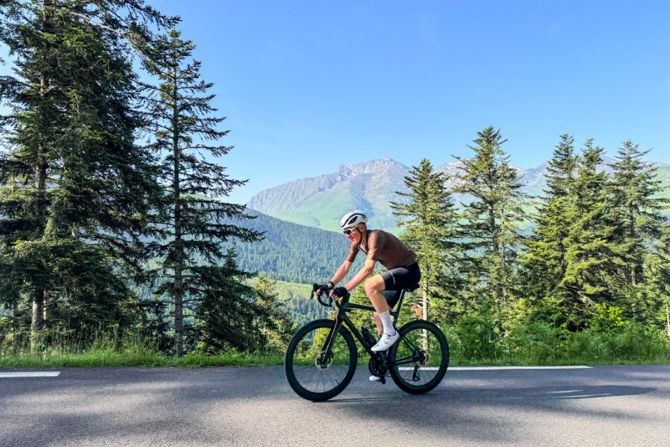 cyclist climbing mountain pass in western pyrenees with trees and mountains backdrop on marmot tours Atlantic to mediterranean pyrenean cycling holiday