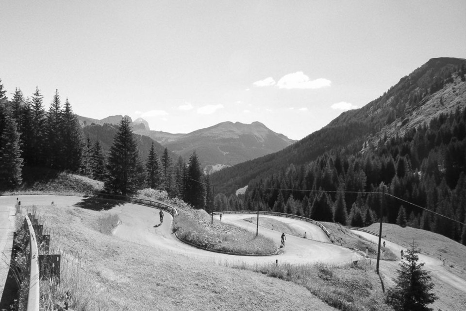 black and white image of pair of cyclists climbing hairpin bends through pasture on guided road cycling tour of Italian dolomites with marmot tours