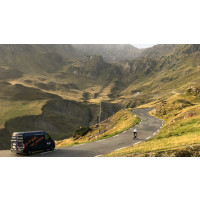 Cyclist climbing Col du Tourmalet cycling climb surrounded by green mountain slopes and passing Marmot Tours support vehicle