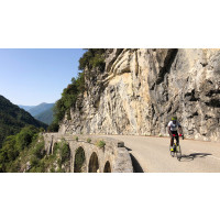 Cyclist on a cliff-hugging road in the mountains in sunshine in southern Alps France on Marmot Tours cycling tour with full support