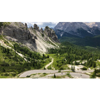 Cyclists on switchbacks on the road to Passo dello Stelvio with rocky mountains and alpine valley views on Marmot Tours cycling holiday with full support