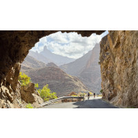 Cyclists on a road under a cliff about to pass through a rock arch with rocky hills behind on Marmot Tours Gran Canaria supported cycling holiday