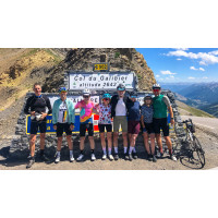 A group of cyclists in colourful kit pose in the sunshine for a photo at the Col du Galibier in the French Alps on a Marmot Tours supported group cycling holiday