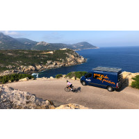A cyclist rides past a Marmot Tours support vehicle parked on a beautiful coast road on Corsica road cycling holiday