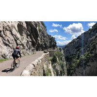 A cyclist rides away from the camera on a road hugging a steep cliff above a gorge on Marmot Tours cycling holiday