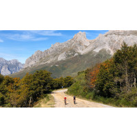Two cyclists side by side on a road through autumn forest with very steep rocky peaks in the backround on Marmot Tours cycling holiday in Picos de Europa