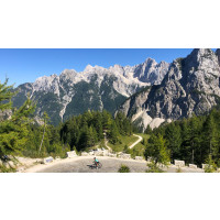 A lone cyclist on an exposed mountain road with very steep forested limestone peaks in the backround on Marmot Tours Slovenia cycling holiday