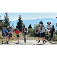 A cyclist stands in the pedals for the final few metres of a tough mountain climb, cheered on by friends at the finish line Marmot Tours group cycling holiday